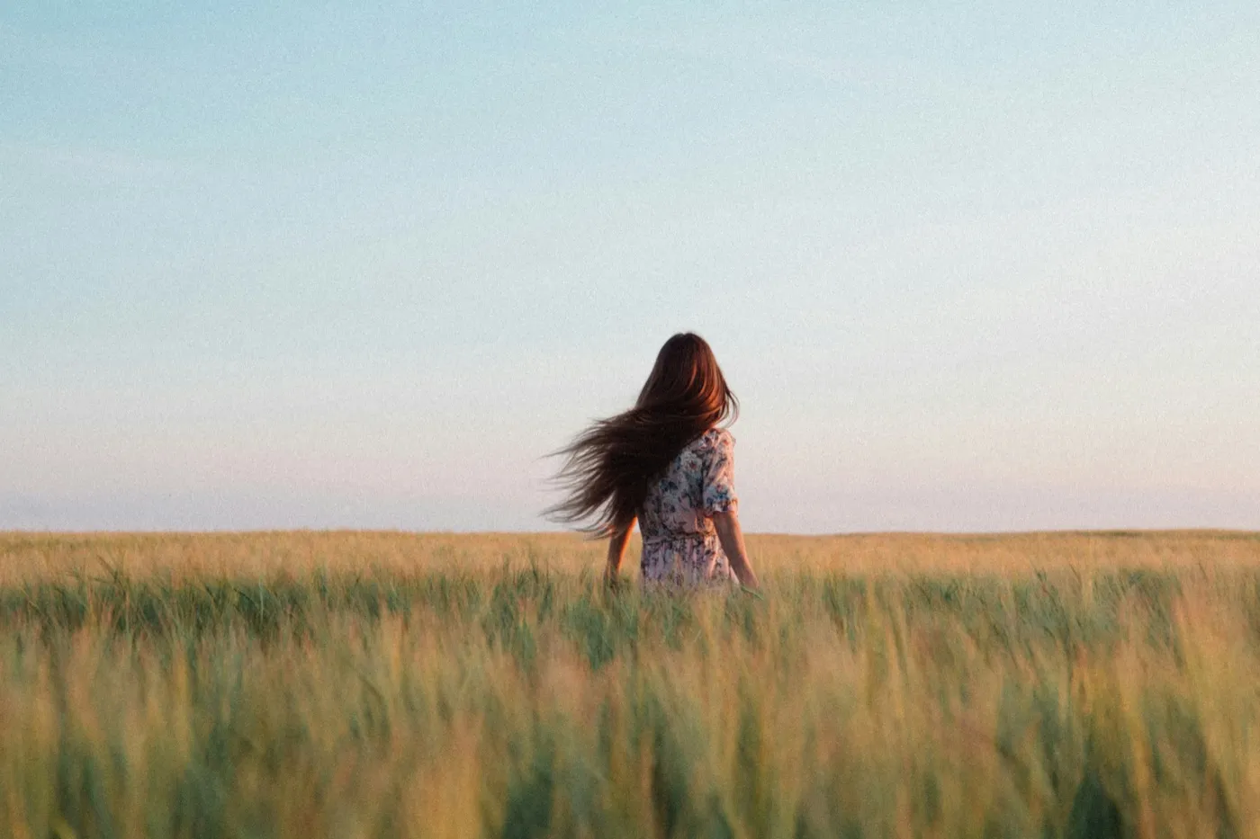 A woman standing peacefully in a golden field at dusk, hair flowing in the breeze